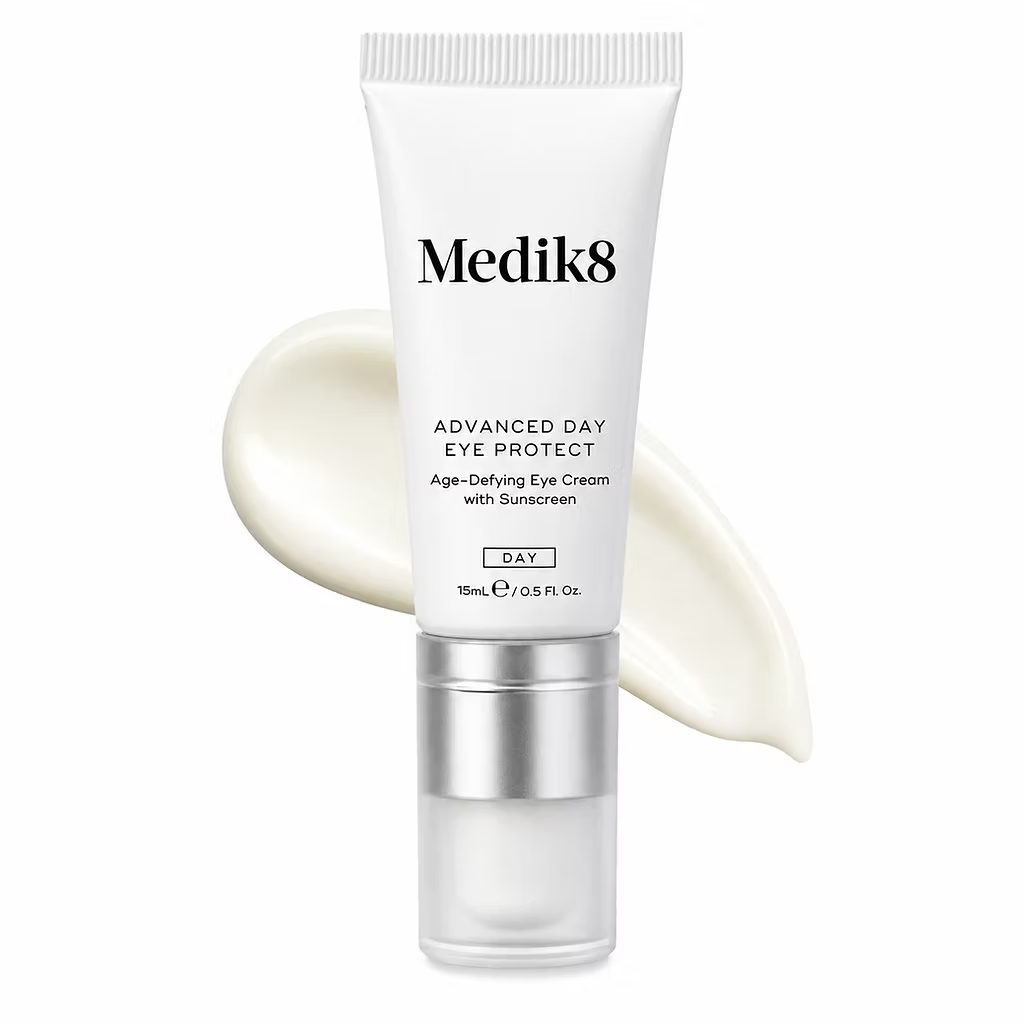 Medik8 Advanced Day Eye Protect 15ml age-defying eye cream with sunscreen in a white tube with silver pump, displayed against a creamy product texture on a white background.