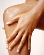 Close-up of hands applying moisturising body cream to a leg during a skincare routine.