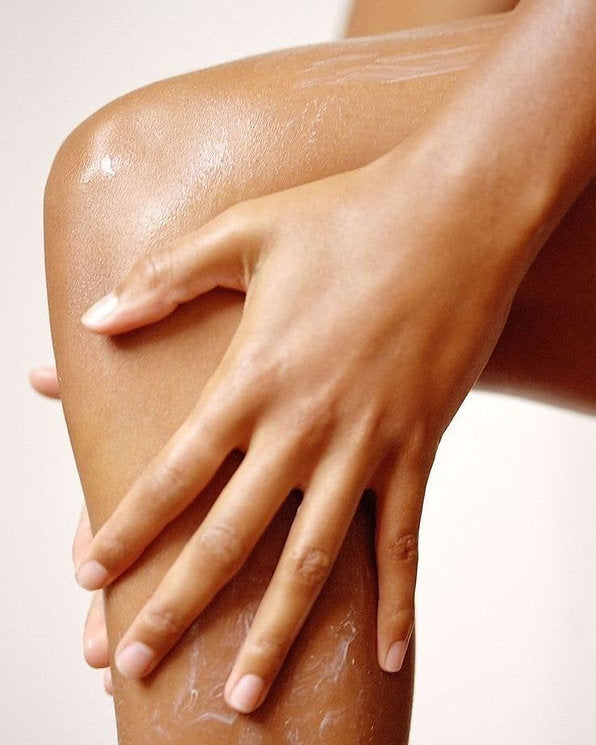 Close-up of hands applying moisturising body cream to a leg during a skincare routine.