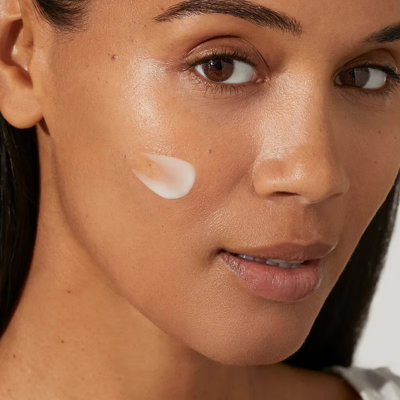 Close-up of a woman applying Medik8 Blemish SOS Rapid Action Target Gel 15ml to her cheek, a targeted skincare treatment for blemish-prone skin.