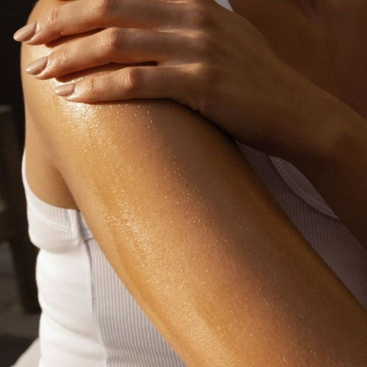 Close-up of a person applying body oil to their  shoulder as part of a nourishing body care routine.