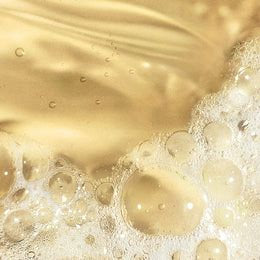 Golden bath and body oil texture with delicate bubbles, illustrating the luxurious sensory experience of Ginger & Me bath & body oil.