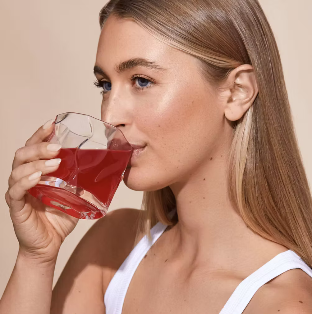 Woman drinking Frank Simple Collagen Beauty Boost pomegranate collagen supplement, formulated with marine and bovine collagen, vitamin C and digestive support ingredients for skin, hair and nail wellness.