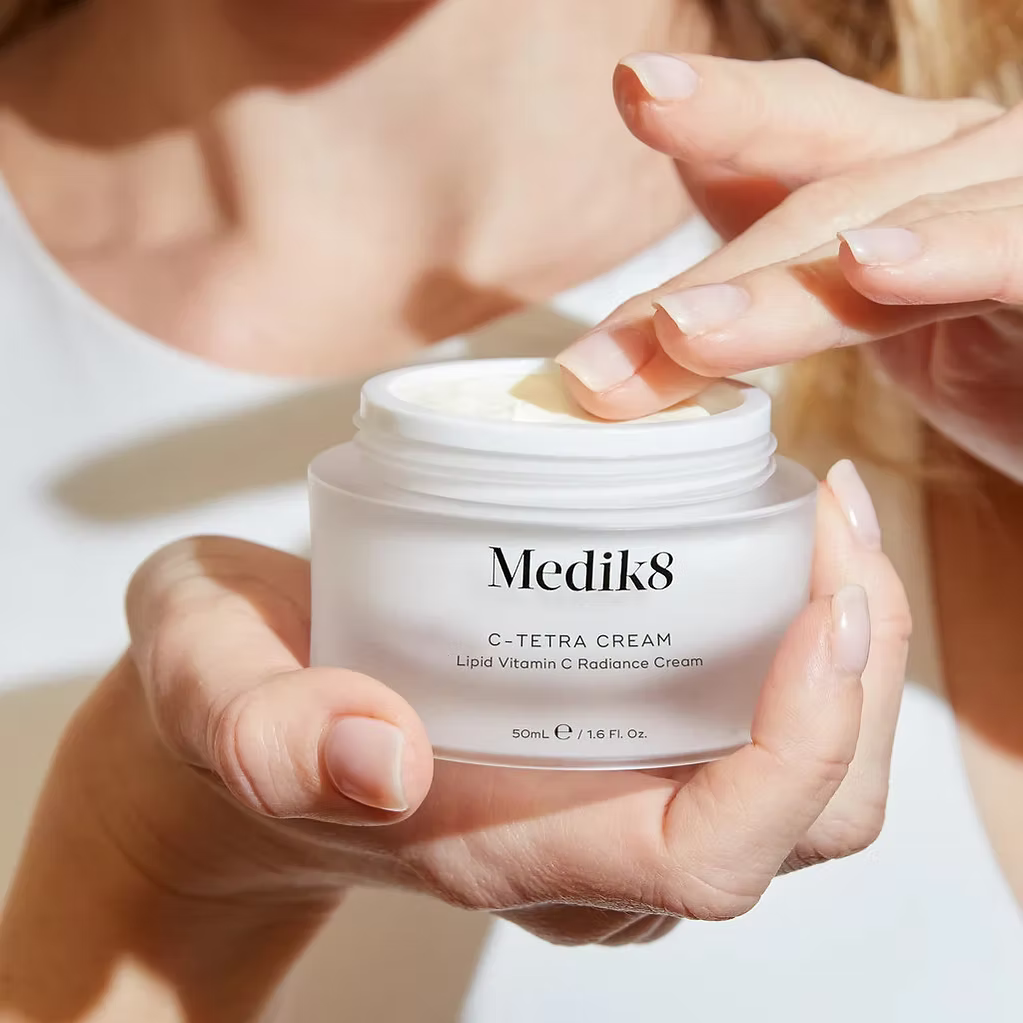 Medik8 C-Tetra Cream 50ml Lipid Vitamin C Radiance Cream being applied with fingertips from an open jar, showcasing its rich, nourishing texture.