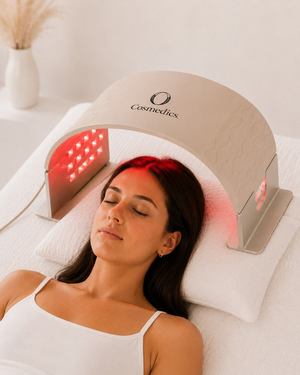 Woman relaxing beneath the O Cosmedics O LED light therapy device, with LED lights illuminating her face and scalp