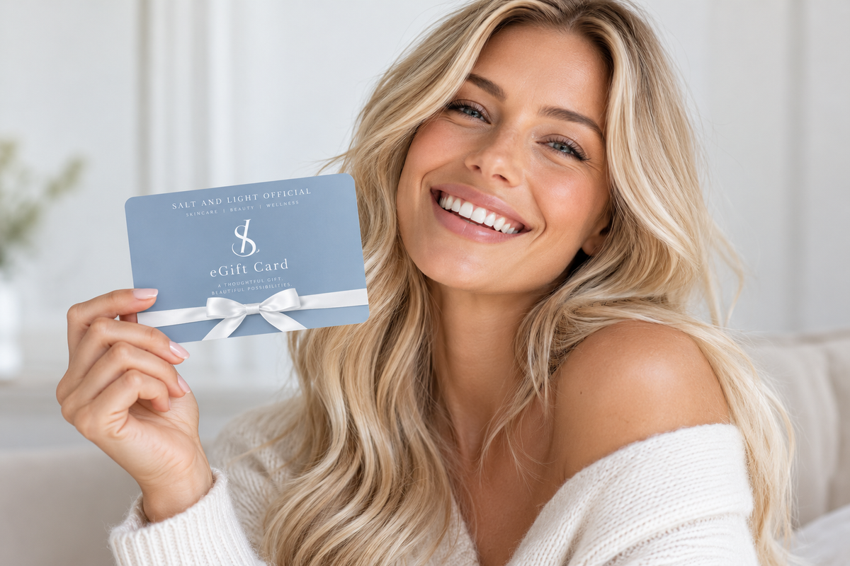 Smiling blonde model holding a Salt and Light Official blue digital gift card with white satin bow, showcasing a luxury skincare and beauty gift voucher.