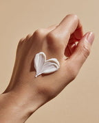 Close-up of a hand with white moisturising cream applied in a heart shape, illustrating hand cream application.