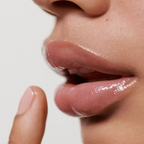 Close-up of glossy, moisturised lips with a fingertip gently touching the lower lip.