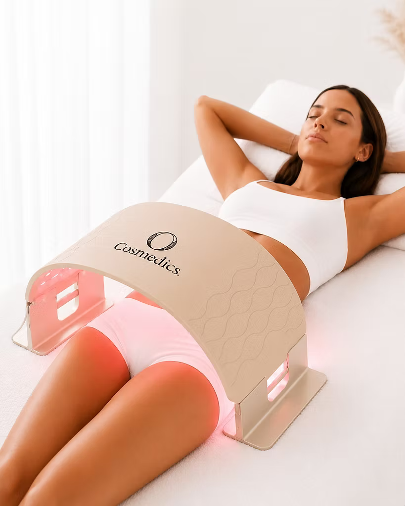 Woman relaxing with the O Cosmedics O LED Light Therapy Device positioned over her hips and upper thighs, demonstrating red LED light therapy for the body.