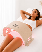 Woman relaxing with the O Cosmedics O LED Light Therapy Device positioned over her hips and upper thighs, demonstrating red LED light therapy for the body.