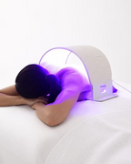 Woman lying face down with the O Cosmedics O LED Light Therapy Device positioned over her upper back and shoulders, demonstrating LED body light therapy.