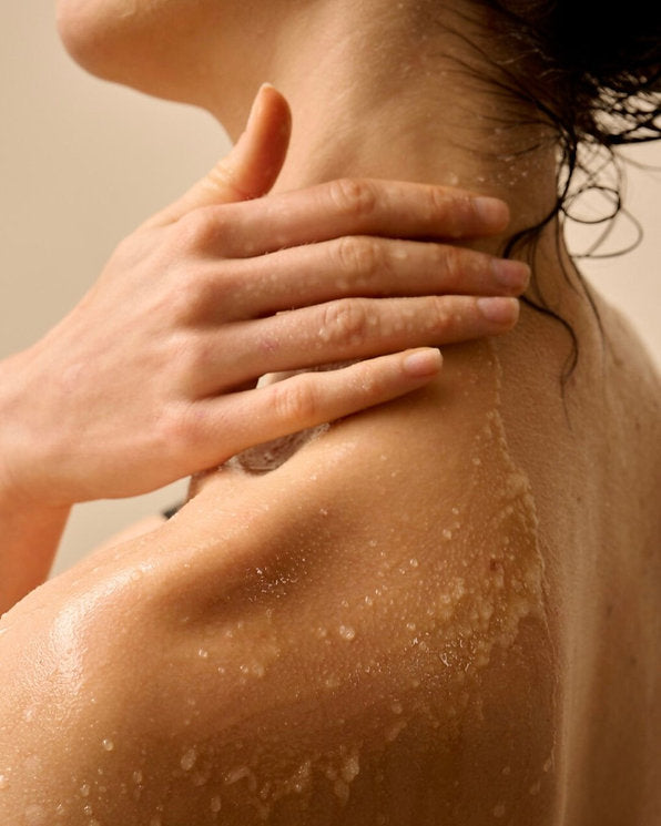 Woman applying Ginger & Me Shower Body Oil to her shoulder, showcasing a nourishing shower oil for soft, hydrated skin.