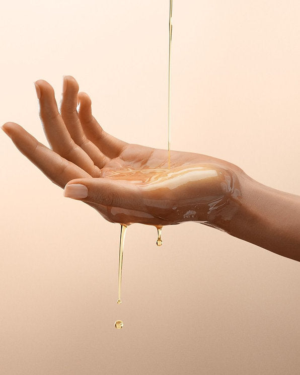 Golden shower body oil being poured into open hands, illustrating the lightweight texture of Ginger & Me Shower Body Oil.