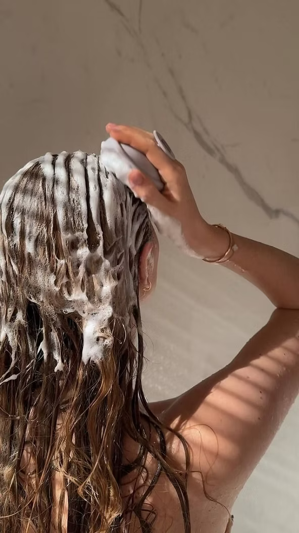 Woman massaging foaming shampoo into wet hair and scalp, demonstrating a hair cleansing routine for healthier, stronger-looking hair with DP Dermaceuticals EXO-GROW Shampoo.