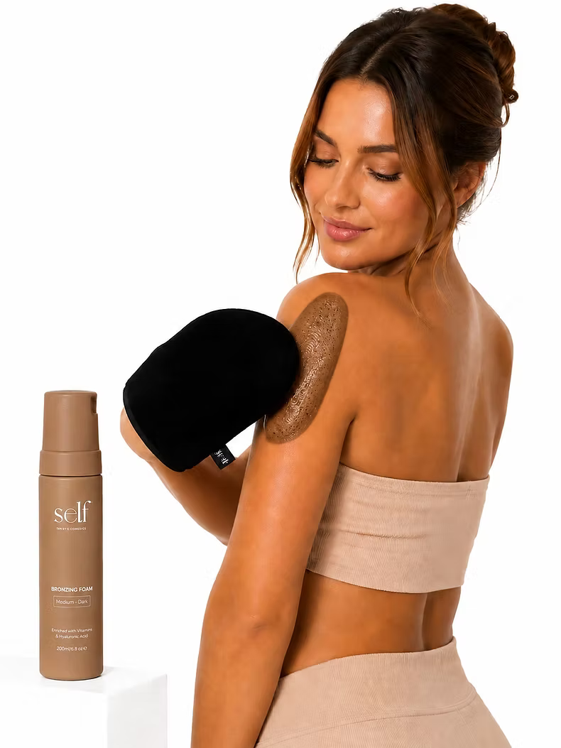 Woman applying self tan to her shoulder using the SELF Tan by O Cosmedics velvet tanning mitt.